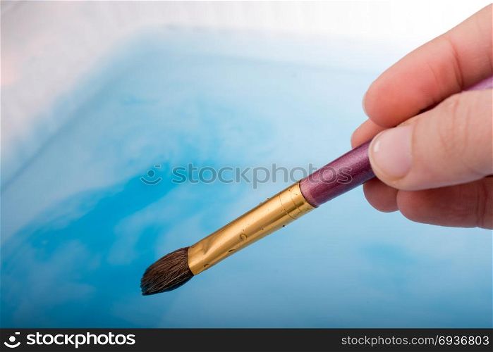 Watercolor paint dissolving in water as painting brush touches water