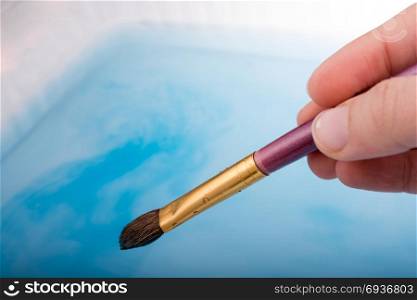 Watercolor paint dissolving in water as painting brush touches water
