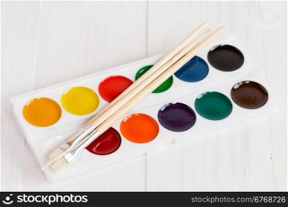 Watercolor paints with set of paint brushes on white wooden background