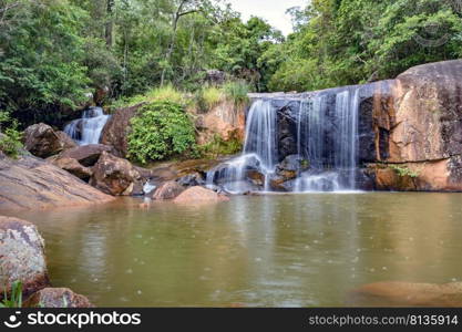 Waterfall and lake in rain forest of Moeda in Minas Gerais state on cloudy day among rocks and vegetation. Cascade and lake in the rain forest between stones