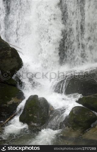 Waterfall consisting of water splashing over many strong boulders in the peaceful forest