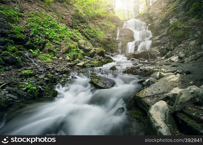 Waterfall in the forest among the black stones. Summer landscape. Waterfall in the forest among black stones
