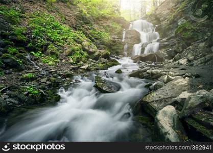 Waterfall in the forest among the black stones. Summer landscape. Waterfall in the forest among black stones