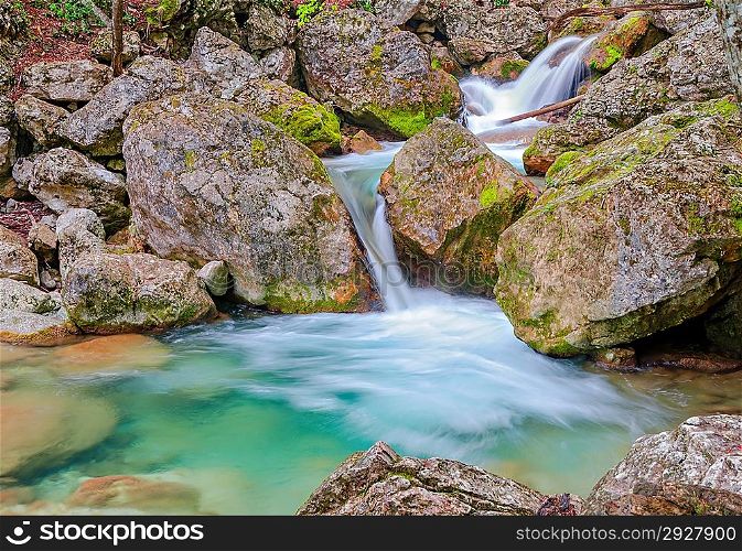 Waterfall in the spring forest. Flow of the spring melt water flowing into the mountain lake