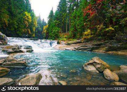 Waterfall on a mountain river with blue water in the forest among bright trees. Waterfall on mountain river with blue water