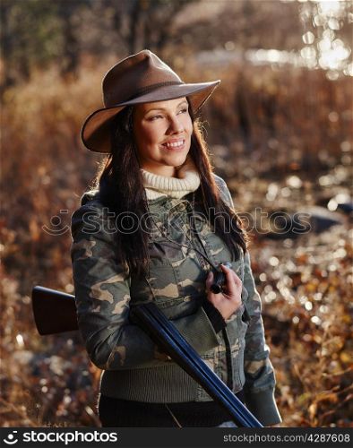 Waterfowl hunting, the female hunter carry a shotgun, autumnal bushes on background