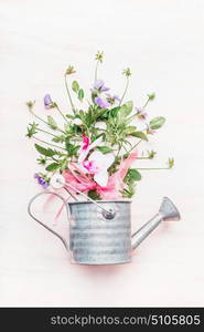 Watering can with bunch of garden flowers on white wooden background, top view