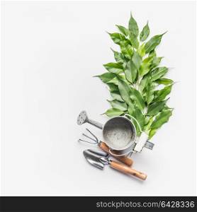 Watering can with gardening tools and green bunch of twigs on white desk background, top view