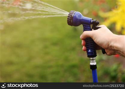 Watering green garden with outdoor hose. hand with hose sprinkle watering plants in the garden. watering lawn or plants on backyard. gardener man with sprinkler in garden.. Watering green garden with outdoor hose. hand with hose sprinkle watering plants in the garden. watering lawn or plants on backyard. gardener man with sprinkler in garden