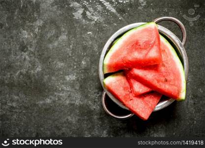 Watermelon chunks in a metal bowl. On the stone table.. Watermelon chunks in a metal bowl.