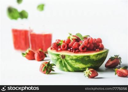 Watermelon halve served with red summer fruits, berries and red juice: strawberries and raspberries  at white background. Healthy summer refreshing. Front view.
