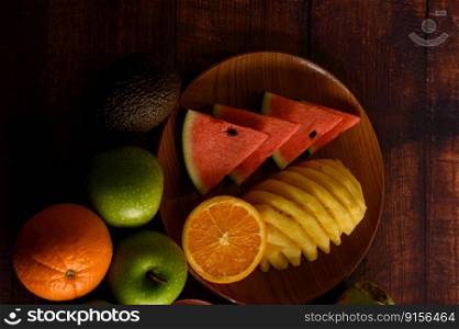 Watermelon, pineapple, oranges, cut into pieces with avocado and apples on wood table. Top view.