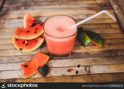 Waternelon and watermelon shake smoothie. Full glass of a creamy and bubbly watermelon shake smoothie with a slice of watermelon and glass tube. Sliced watermelon and paper decorative on brown wood board background in rustic style.