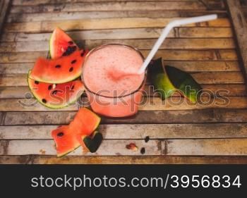 Waternelon and watermelon shake smoothie. Full glass of a creamy and bubbly watermelon shake smoothie with a slice of watermelon and glass tube. Sliced watermelon and paper decorative on brown wood board background in rustic style.