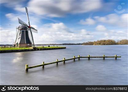 Waterways of Holland and view on traditional Dutch wind mill, Dutch lifestyle landscape. Passing clouds above dutch windmill that stands on the edge of the lake