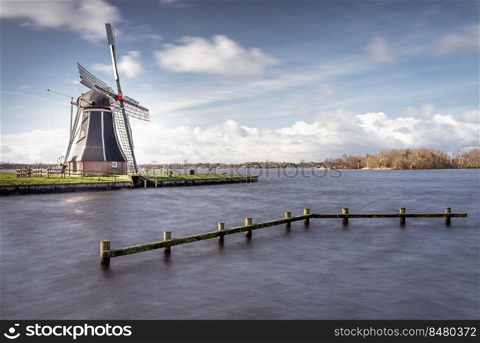 Waterways of Holland and view on traditional Dutch wind mill, Dutch lifestyle landscape. Dutch windmill at a lake with dynamic cloudscape