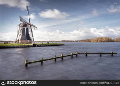 Waterways of Holland and view on traditional Dutch wind mill, Dutch lifestyle landscape. Dutch windmill at a lake with dynamic cloudscape