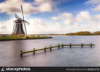 Waterways of Holland and view on traditional Dutch wind mill, Dutch lifestyle landscape. Typical Dutch landscape with cumulus clouds and traditional windmill on the waterfront