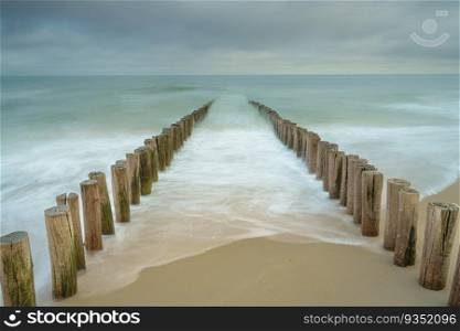 Wave breakers on the beach of Domburg in the Netherlands. Long exposure photo with dynamic waves breaking at the shore on wooden poles. Wooden breakwater poles in the waves of the nord sea
