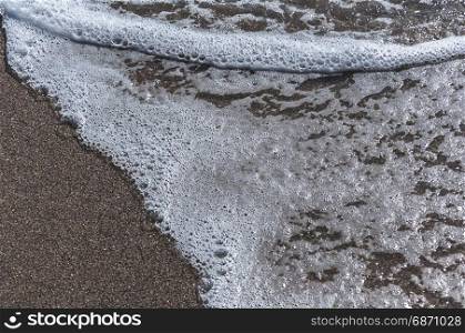 Wave with foam on a sandy beach