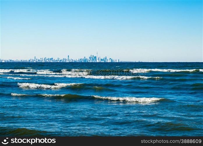 Waves breaking on azure water on Lake Ontario, against clear blue sky with Toronto city skyline far in distance.