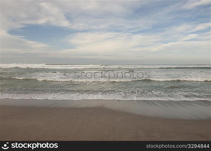 Waves breaking on the beach under a cloudy blue sky