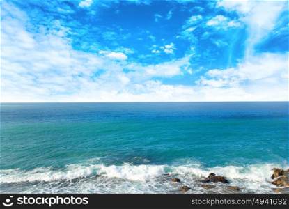 Waves breaking the shore at blue sea and sky with white clouds