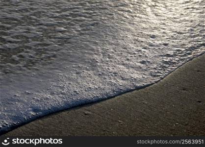 Waves coming ashore, at sunset, beach and foam.