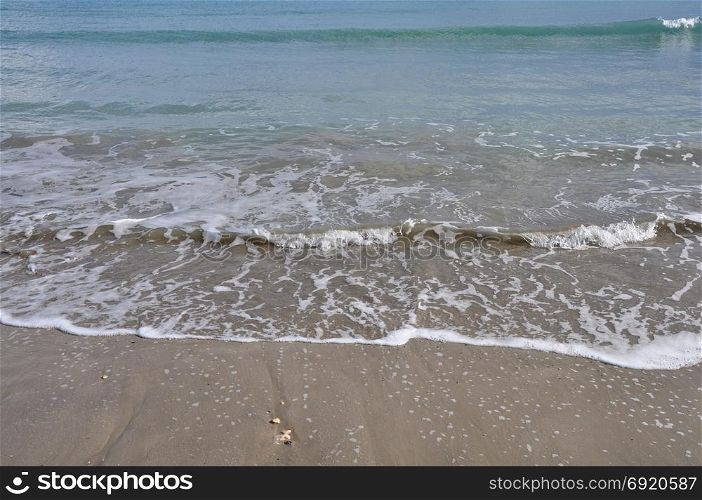 Waves crashing on sandy beach. Waters edge abstract sea background.