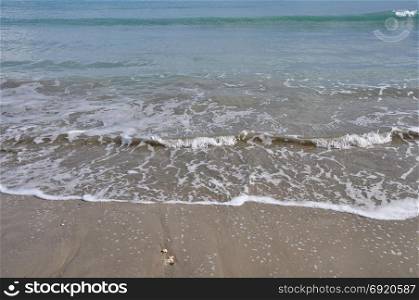 Waves crashing on sandy beach. Waters edge abstract sea background.