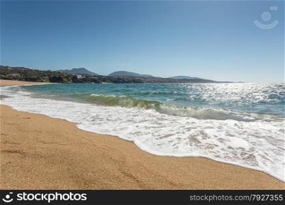 Waves gently lapping onto the beach at Propriano with golden sand, blue sea and blue sky and hills in the background