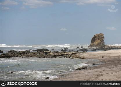Waves lapping up against a sandy beach with an outcropping of rocks, and a stack in the background