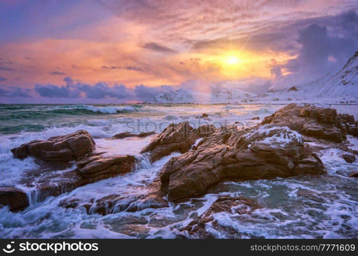 Waves of Norwegian sea on rocky coast in fjord on sunset with sun. Skagsanden beach, Lofoten islands, Norway. Norwegian Sea waves on rocky coast of Lofoten islands, Norway