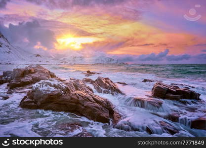 Waves of Norwegian sea on rocky coast in fjord on sunset with sun. Skagsanden beach, Lofoten islands, Norway. Norwegian Sea waves on rocky coast of Lofoten islands, Norway