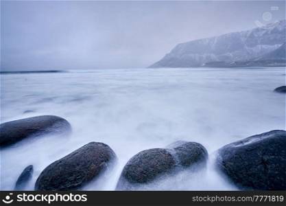 Waves of Norwegian sea surging on stone rocks at Unstad beach, Lofoten islands, Norway in winter storm. Long exposure. Waves of Norwegian sea surging on stone rocks. Long exposure