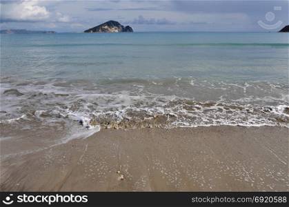 Waves splashing on sandy beach Keri in Zakynthos Greece and Marathonisi island natural habitat of the caretta-caretta sea turtle.