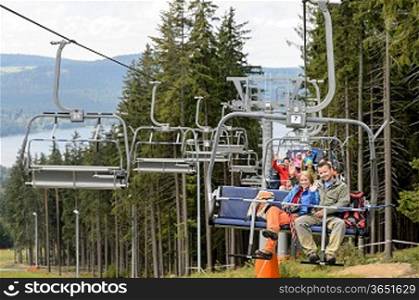 Waving young people sitting on chairlift going through forest