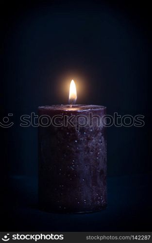 Wax candle with a burning light on a dark background. Candle Black Background