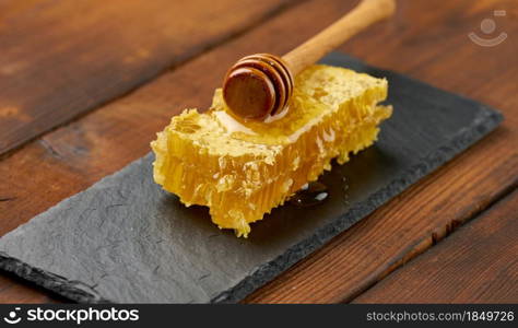 wax honeycomb with honey on a black board and a wooden spoon, brown table