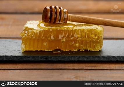 wax honeycomb with honey on a black board and a wooden spoon, brown table