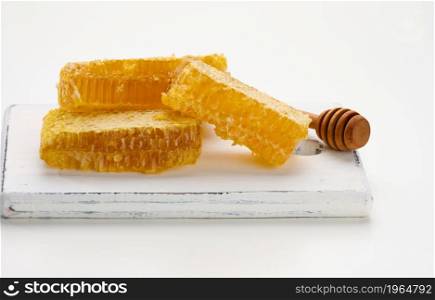 wax honeycomb with honey on a white board and a wooden spoon