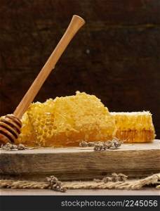 wax honeycomb with honey on wooden board and wooden spoon, brown table