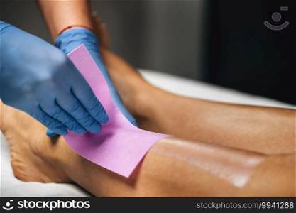 Waxing procedure, beautician wearing protective gloves applies depilation wax to female legs ina beauty center.. Waxing Legs Procedure in a Beauty Center