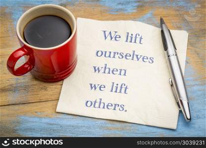 We lift ourselves by lifting others. We lift ourselves by lifting others - inspiraitonal handwriitng on napkin with a cup of coffee