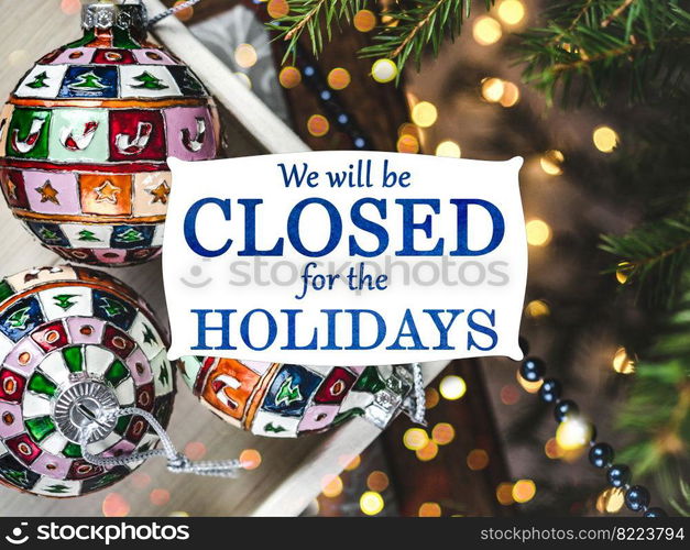 We will be closed for the Holidays. Beautiful signboard for Christmas and New Year holidays. Colorful Christmas balls on the background of the Christmas tree. Closeup, top view. Holidays concept. We will be closed for the Holidays