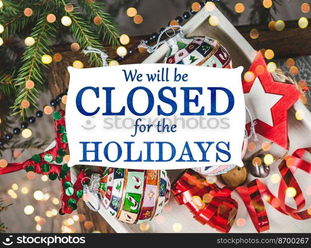 We will be closed for the Holidays. Beautiful signboard for Christmas and New Year holidays. Colorful Christmas balls on the background of the Christmas tree. Closeup, top view. Holidays concept. We will be closed for the Holidays