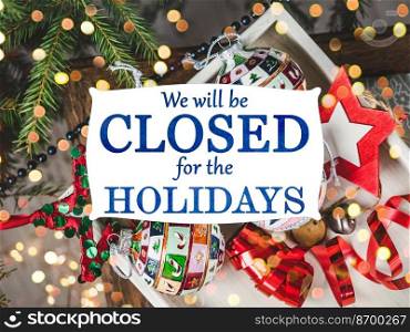 We will be closed for the Holidays. Beautiful signboard for Christmas and New Year holidays. Colorful Christmas balls on the background of the Christmas tree. Closeup, top view. Holidays concept. We will be closed for the Holidays