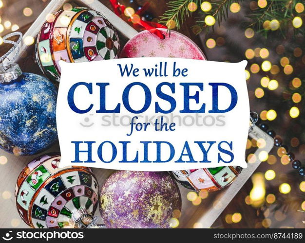 We will be closed for the Holidays. Beautiful signboard for Christmas and New Year holidays. Colorful Christmas balls on the background of the Christmas tree. Closeup, top view. Holidays concept. We will be closed for the Holidays