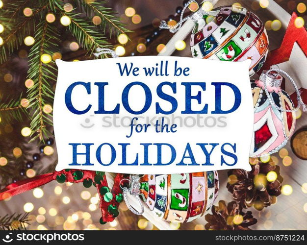 We will be closed for the Holidays. Beautiful signboard for Christmas and New Year holidays. Colorful Christmas balls on the background of the Christmas tree. Closeup, top view. Holidays concept. We will be closed for the Holidays