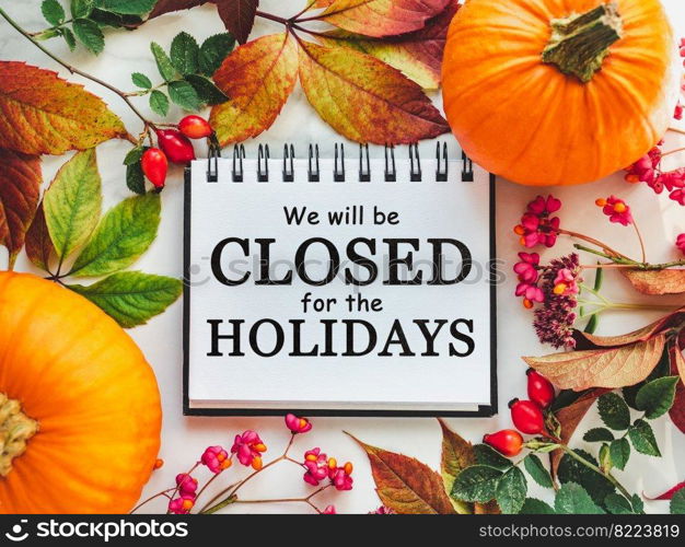 We will be closed for the Holidays. Beautiful Thanksgiving sign. Bright pumpkins, tree leaves, red berries and colorful flowers lying on an empty table. Close-up, top view. Holiday concept. We will be closed for the Holidays. Thanksgiving sign